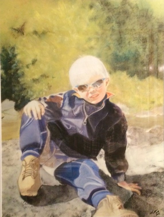 A toddler in sunglasses and a dark jacket sitting on rocks outdoors.