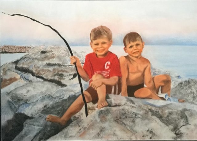Two young brothers sitting on lakeshore rocks, one holding a stick as a fishing pole.