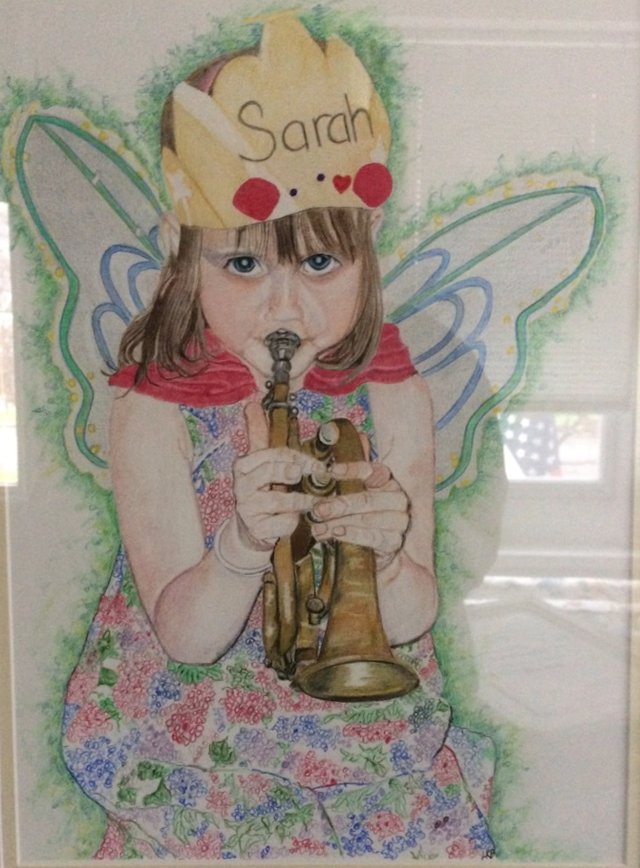 A little girl wearing fairy wings and a paper crown, playing a small brass horn.