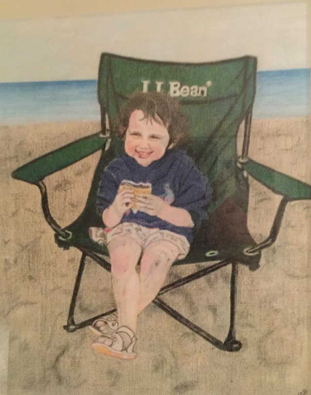 A small child in a green folding beach chair by the water, holding a s'more.