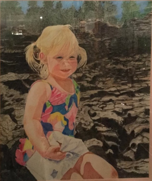 A little girl with blond pigtails in a colorful swimsuit, sitting on dark rocks.