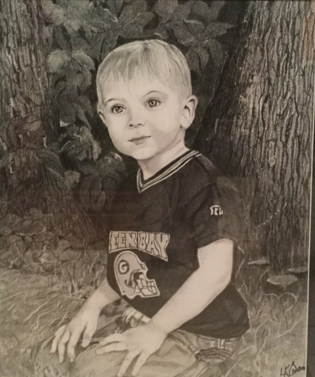 A young boy in a Green Bay football jersey sitting at the foot of a tree, drawn in graphite.